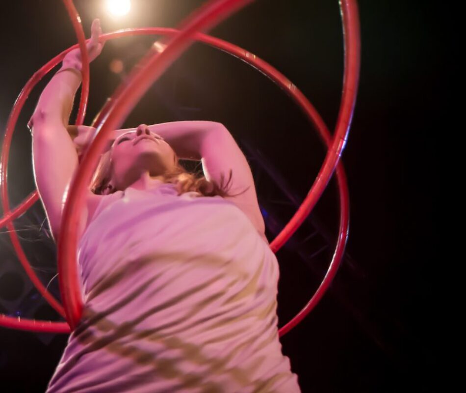 Annika Hakala hulahoop artist performing on stage in Vienna with multiple pink hulahoops. Close shot from down in lilac setting. Theater stage.