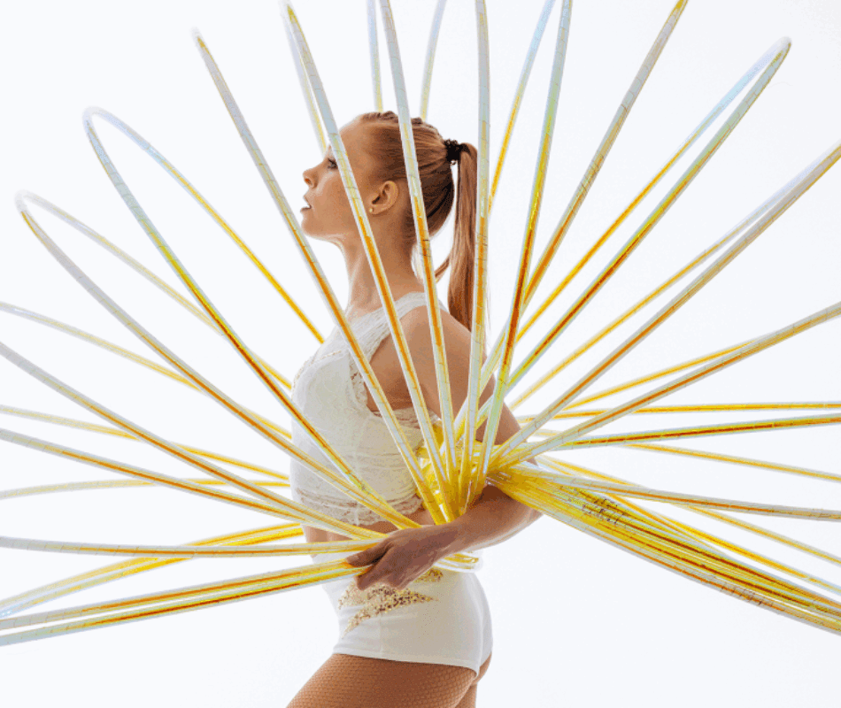 Hulahoop artist Annika Hakala pictured from the side in an elegant pose with multiple golden hulahoops spread like a fan around her upper body. White background.