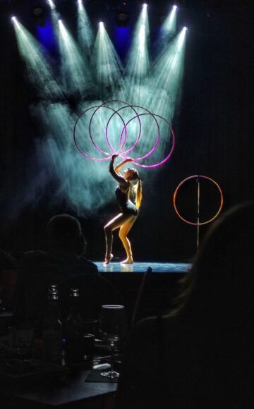 Hulahoop artist Annika Hakala on stage in Papierfabrik Variete with 4 hula hoops. Dark background and pink hula hoops.